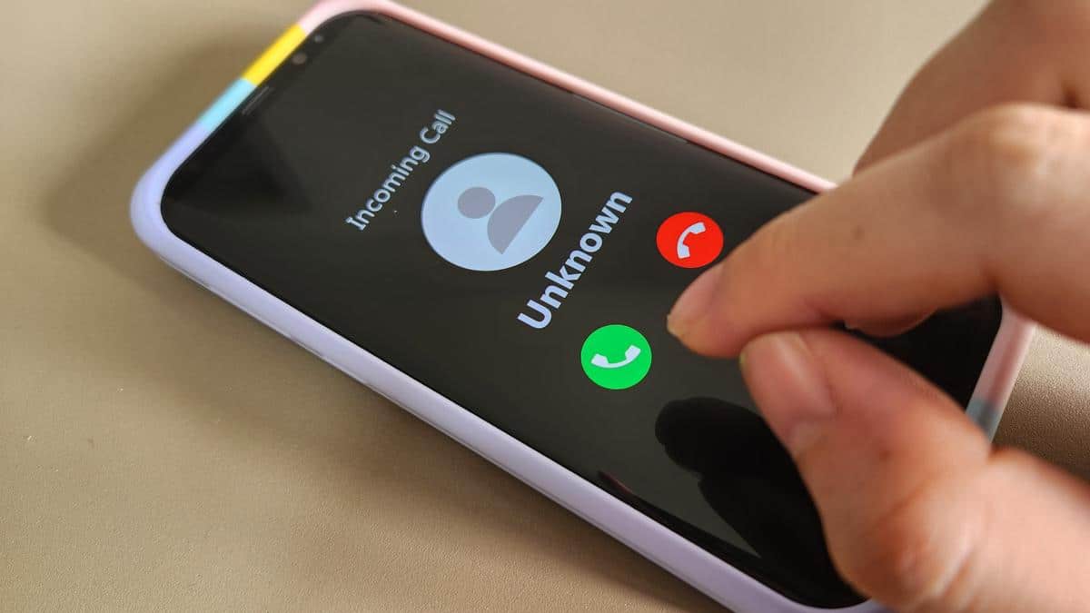 A person answers a phone where the caller ID screen reads “Unknown”.