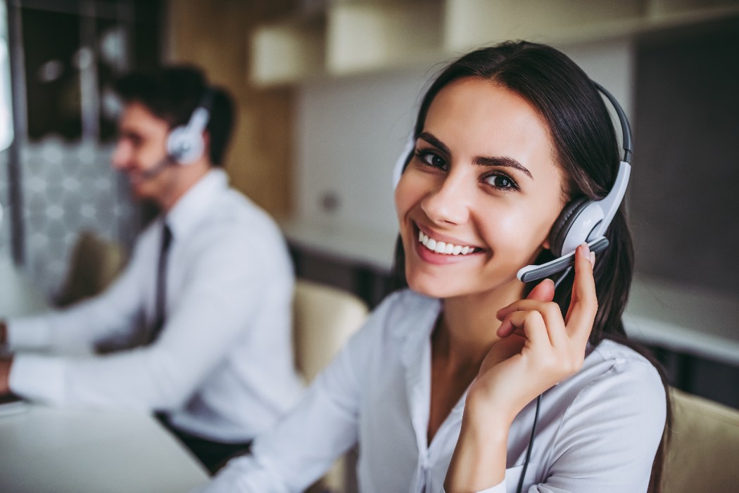Two call center agents, one a woman smiling while the other is a man in the background. 