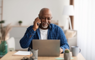 man talking on the phone smiling while also on laptop