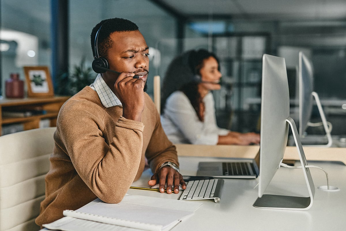 A call center agent looks thoughtfully at his computer, thinking hard about where to transfer an incoming caller.