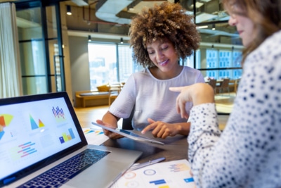 2 colleagues discussing customer focus while sitting at their computers.