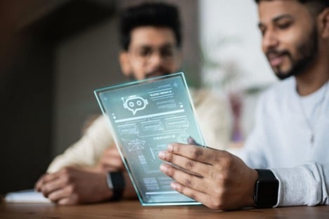 Two people are looking at a transparent tablet with a digital interface displaying diagrams and an icon for AI chatbots for customer service