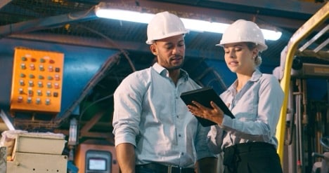 Engineers in an industrial environment conduct business while consulting a document on a tablet.