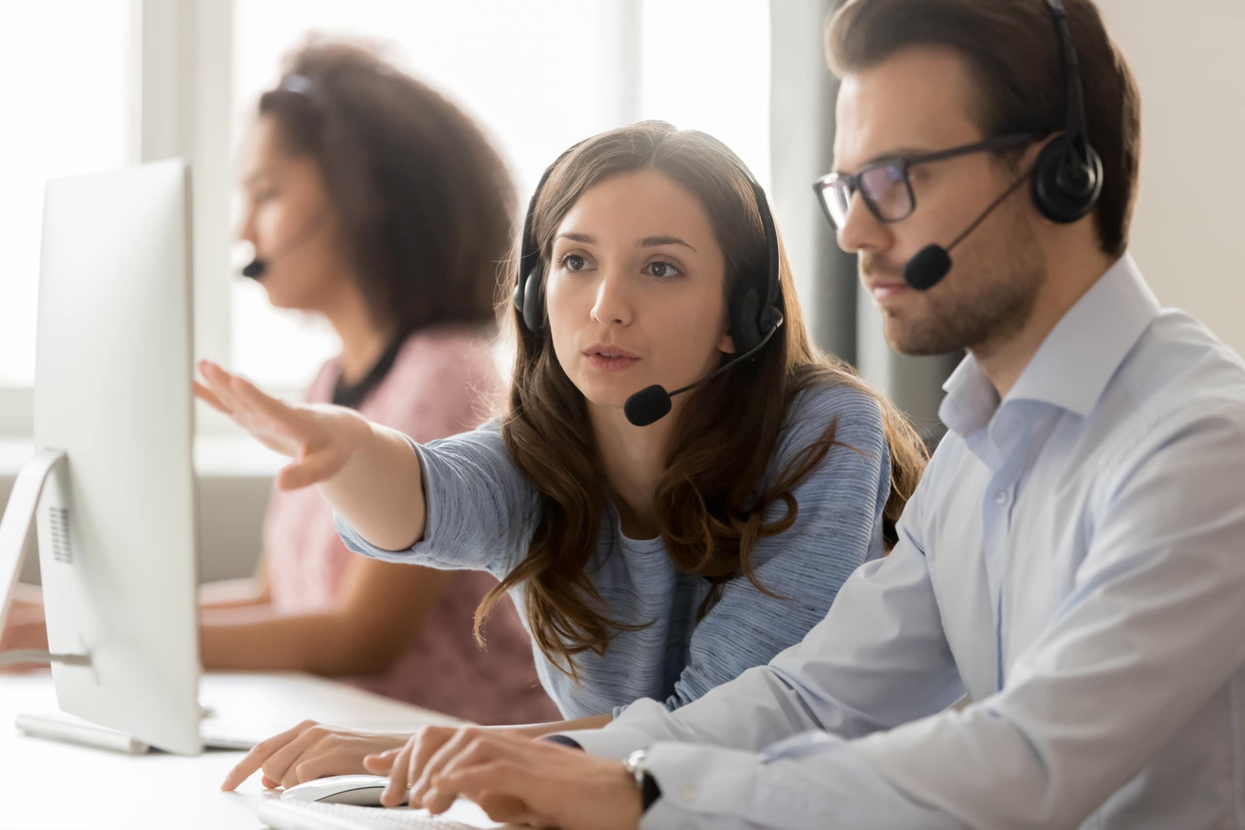 A call center supervisor works closely with an agent to implement new speech analytics software