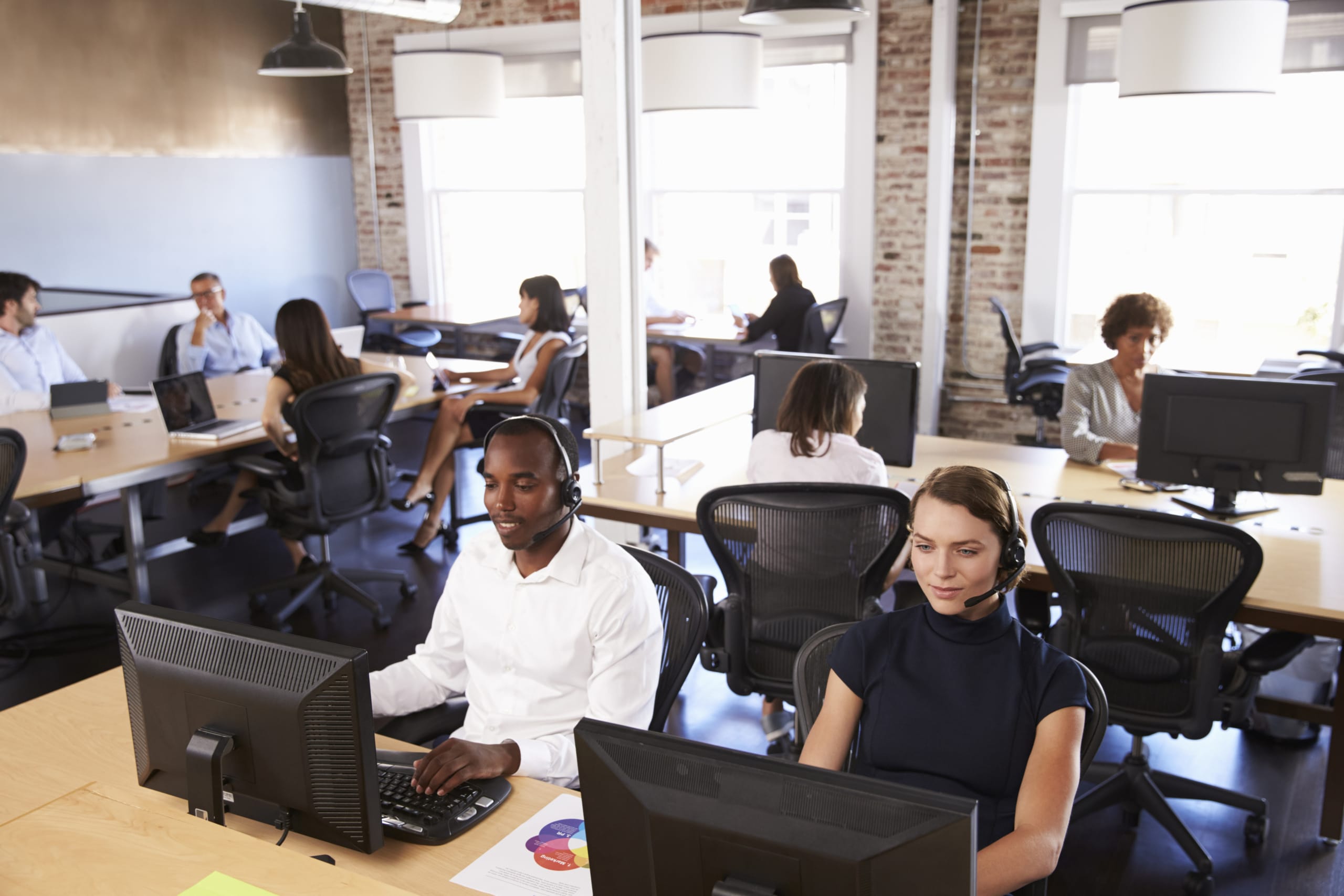 Several call center agents taking calls in a busy open-concept office.