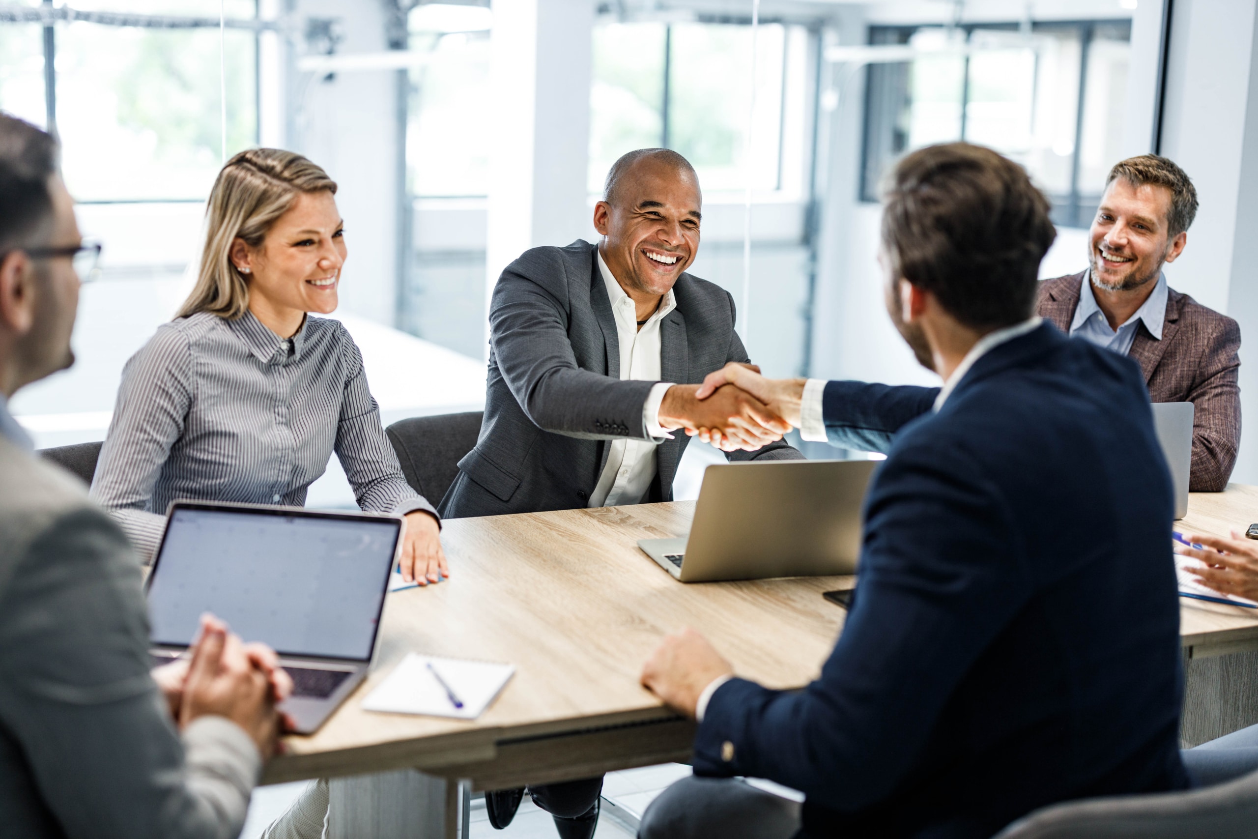 A group of business leaders make an agreement with their new outbound call center outsourcing partner, shaking hands in a business meeting.