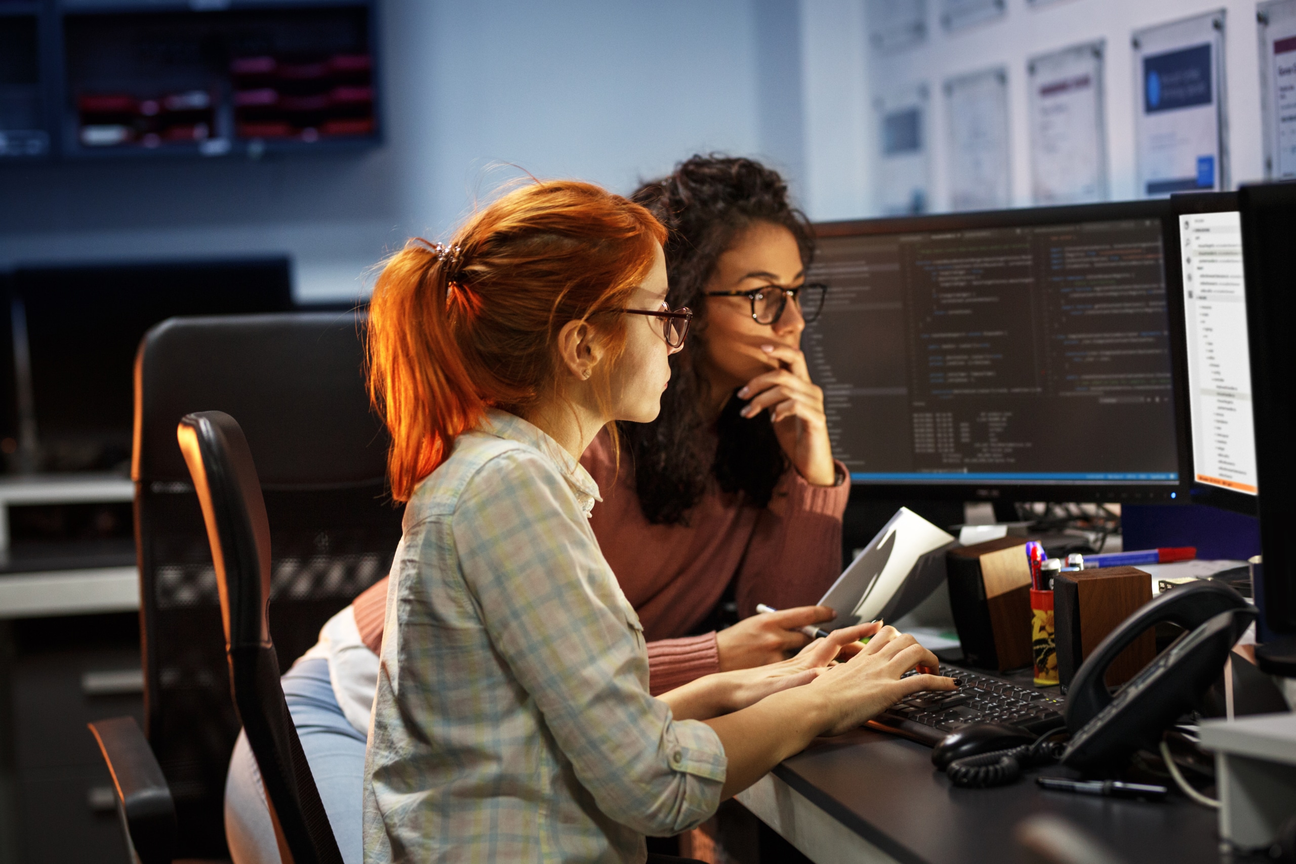 Two programmers huddle around a workstation, thinking intently about how to properly implement an AI contact center tool.