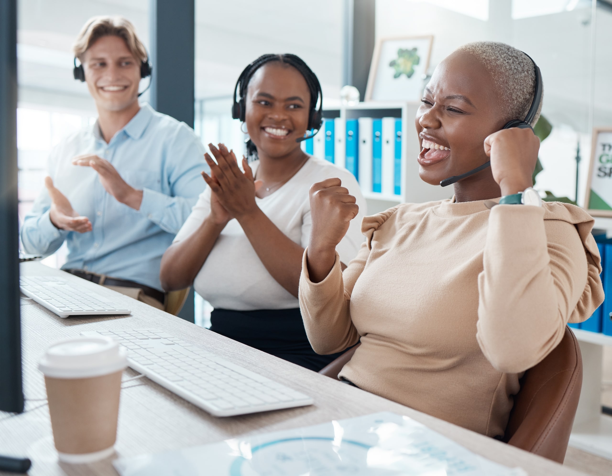 Three call center agents celebrating agent accomplishment at desk