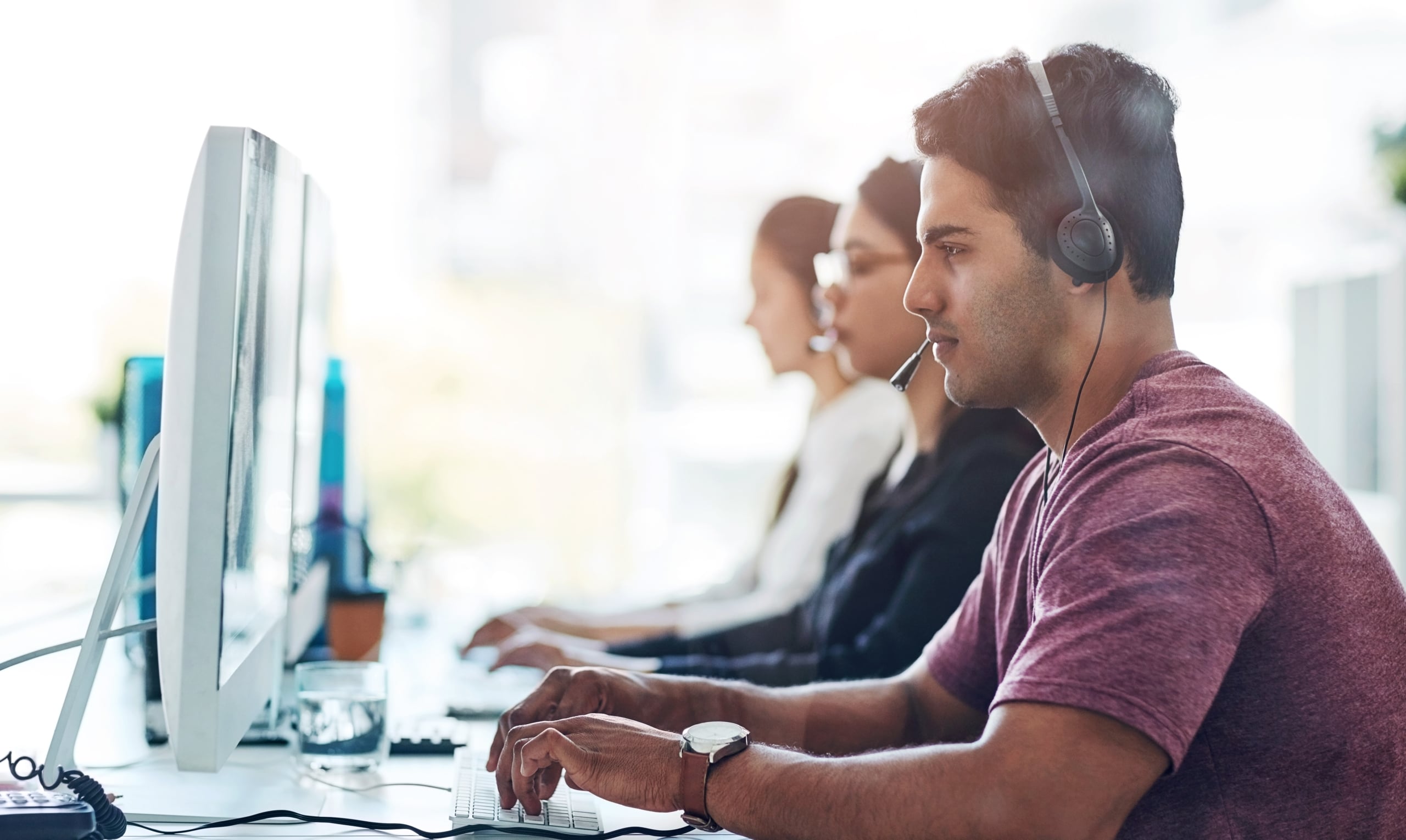 three contact center agents sitting in a row in front of computers, talking on headsets