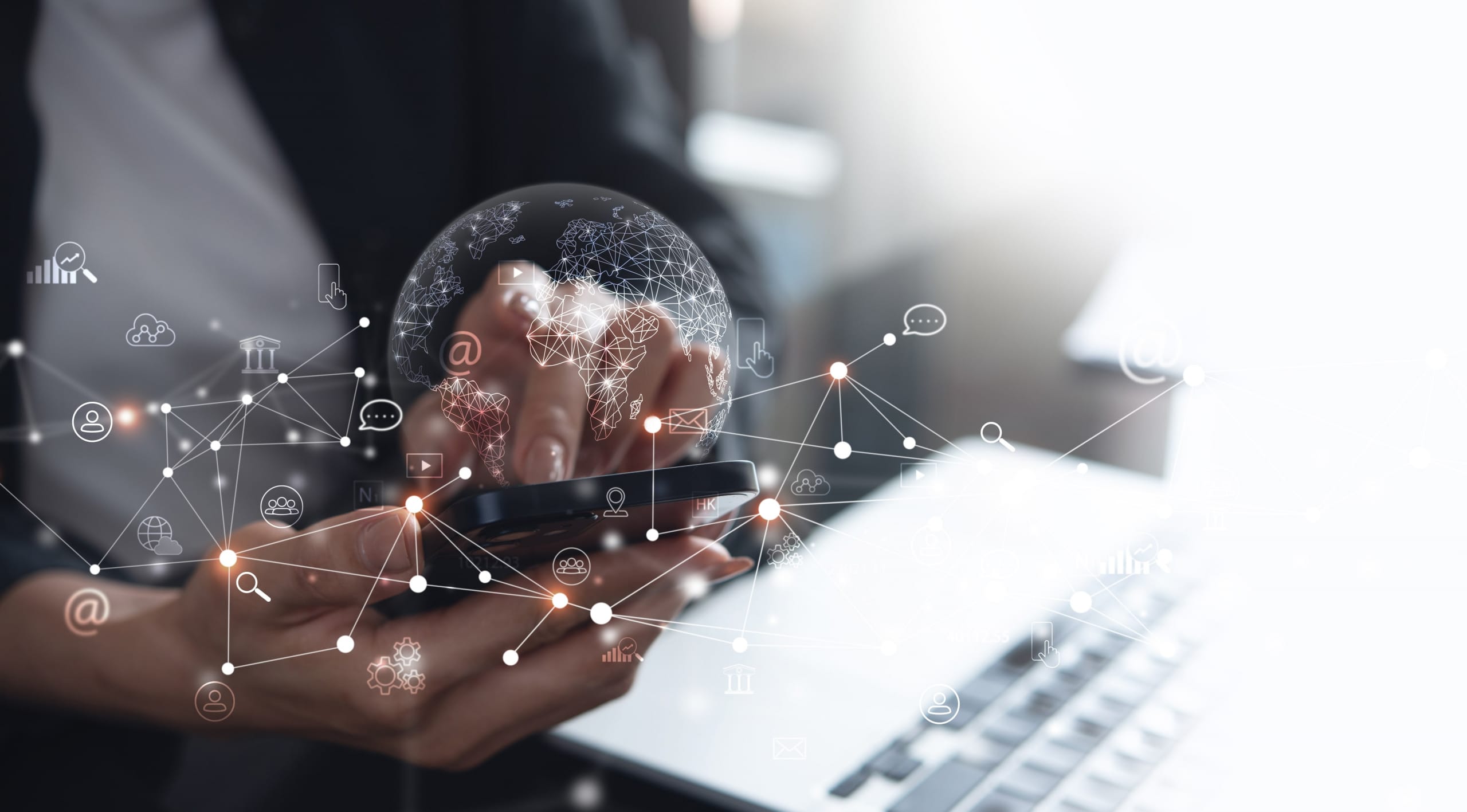 A close-up of hands holding smart phone in front of a laptop, with a web of interconnected dots and a globe of the earth superimposed.