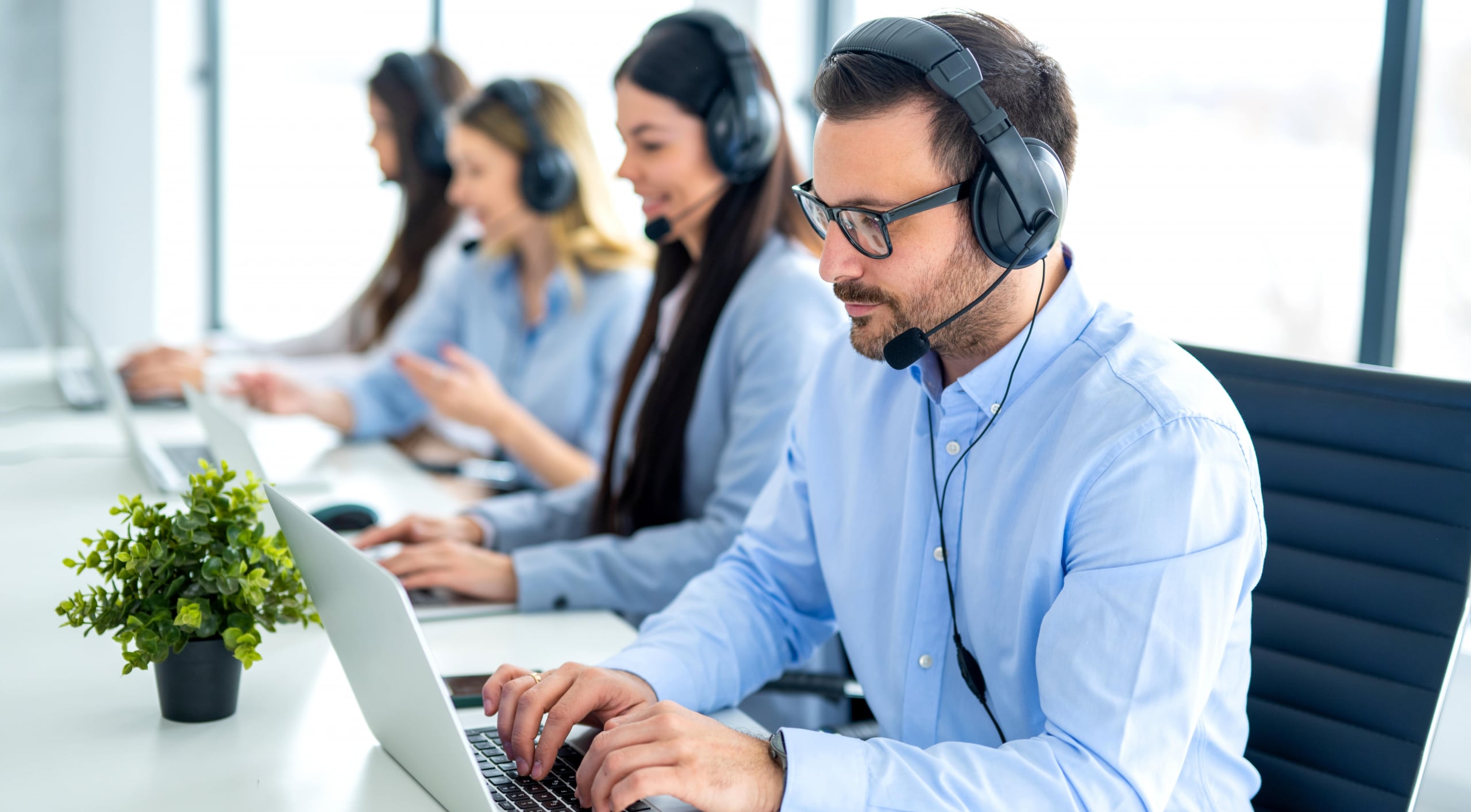 Call center agents wearing headsets and typing on laptops at a desk.