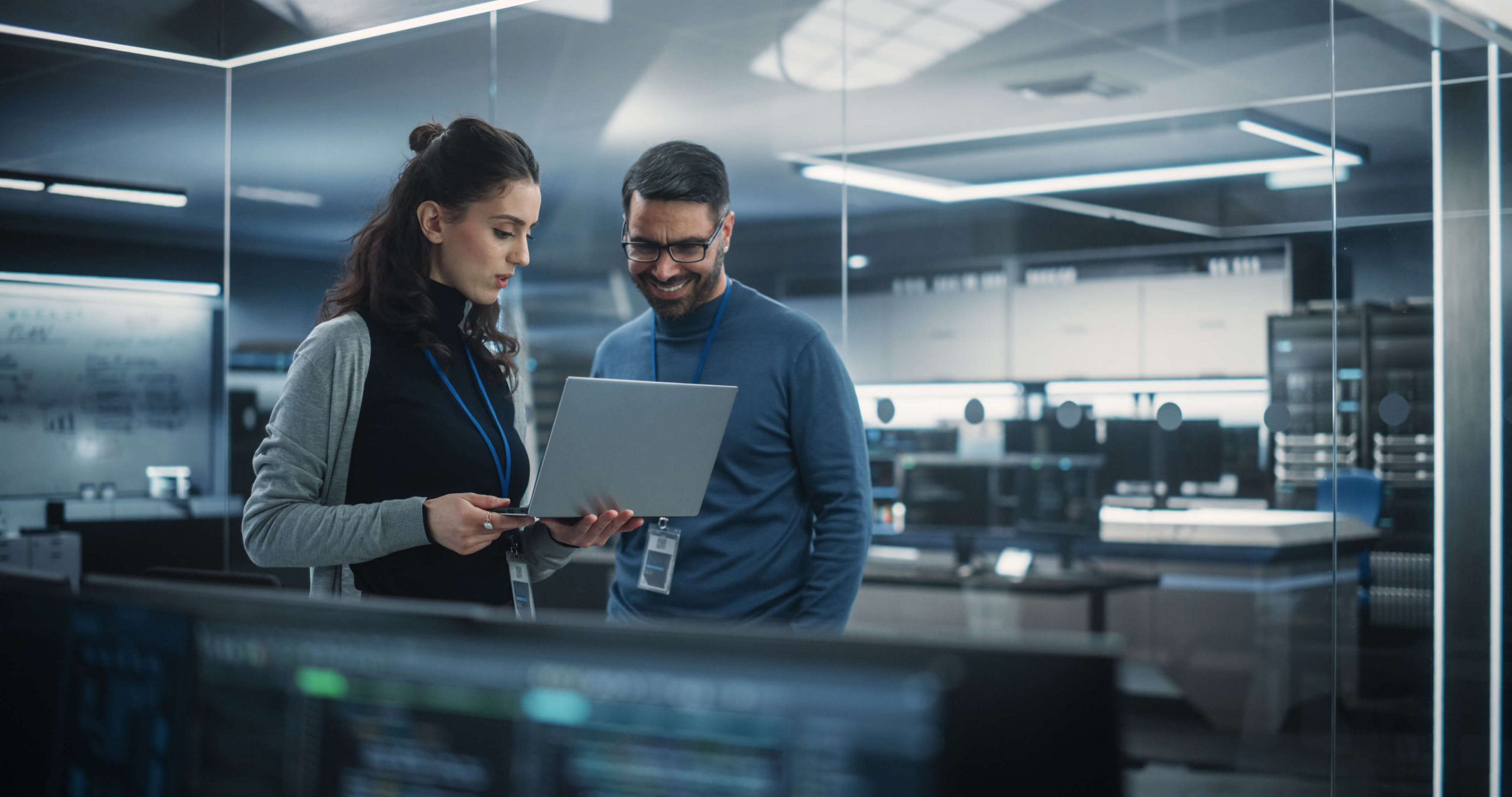 a young female and young male co worker with a laptop standing in an open office