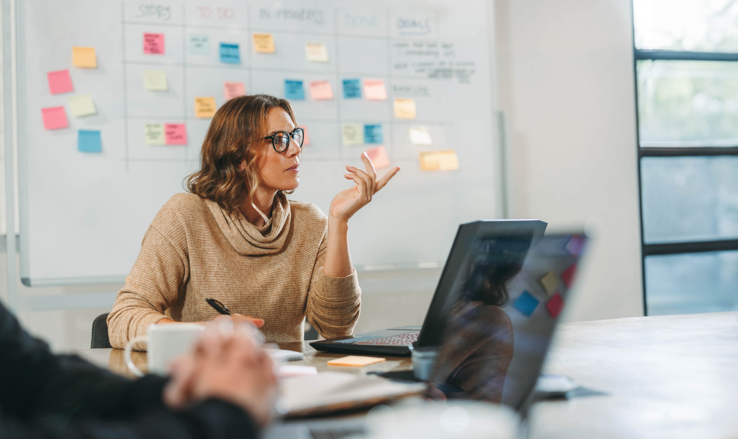 Woman engaging in a collaborative brainstorming session with her colleagues in a boardroom. Business people discuss ideas and manage projects. They work together on software development.