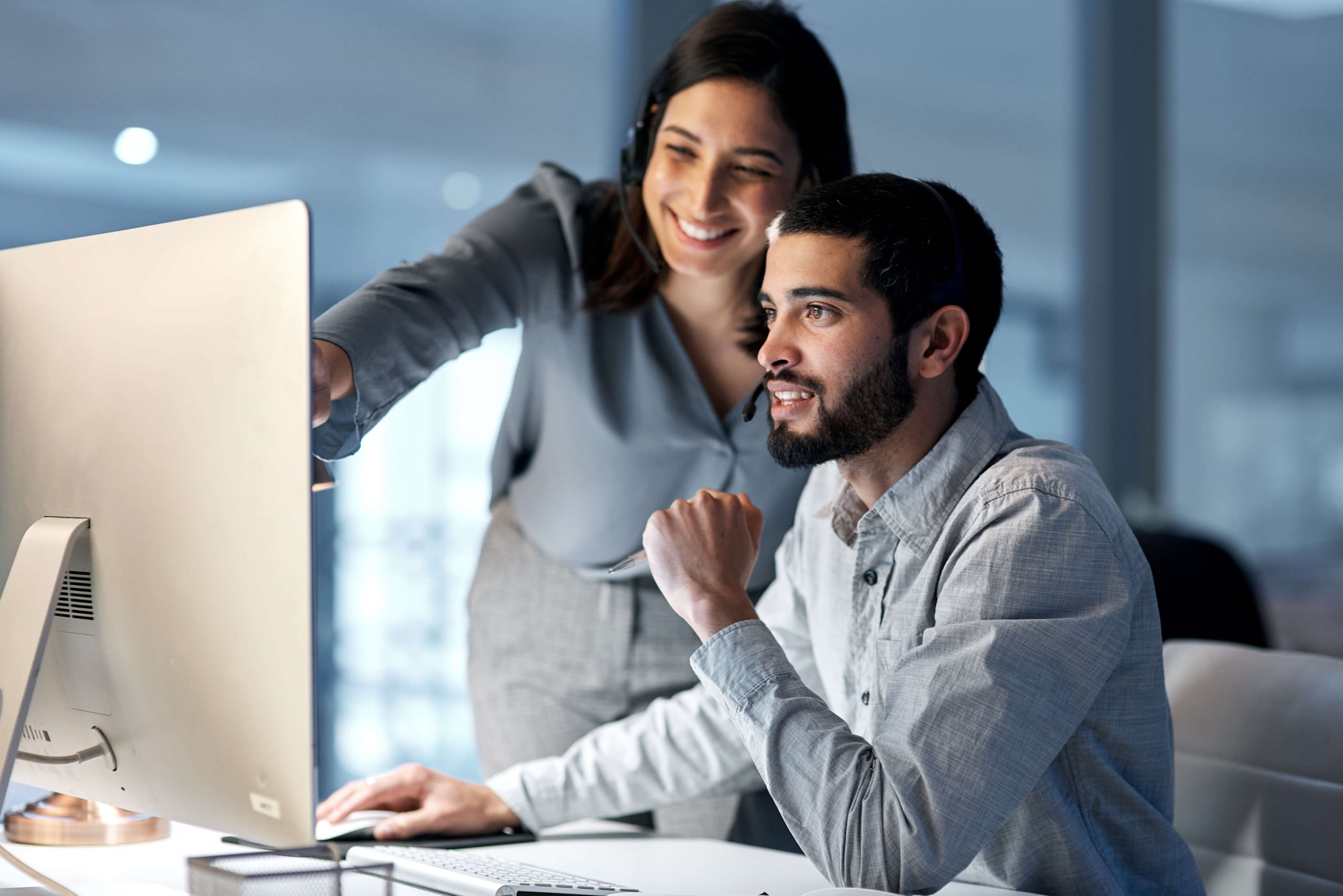 Smiling male and female help desk coworkers pointing at a computer screen