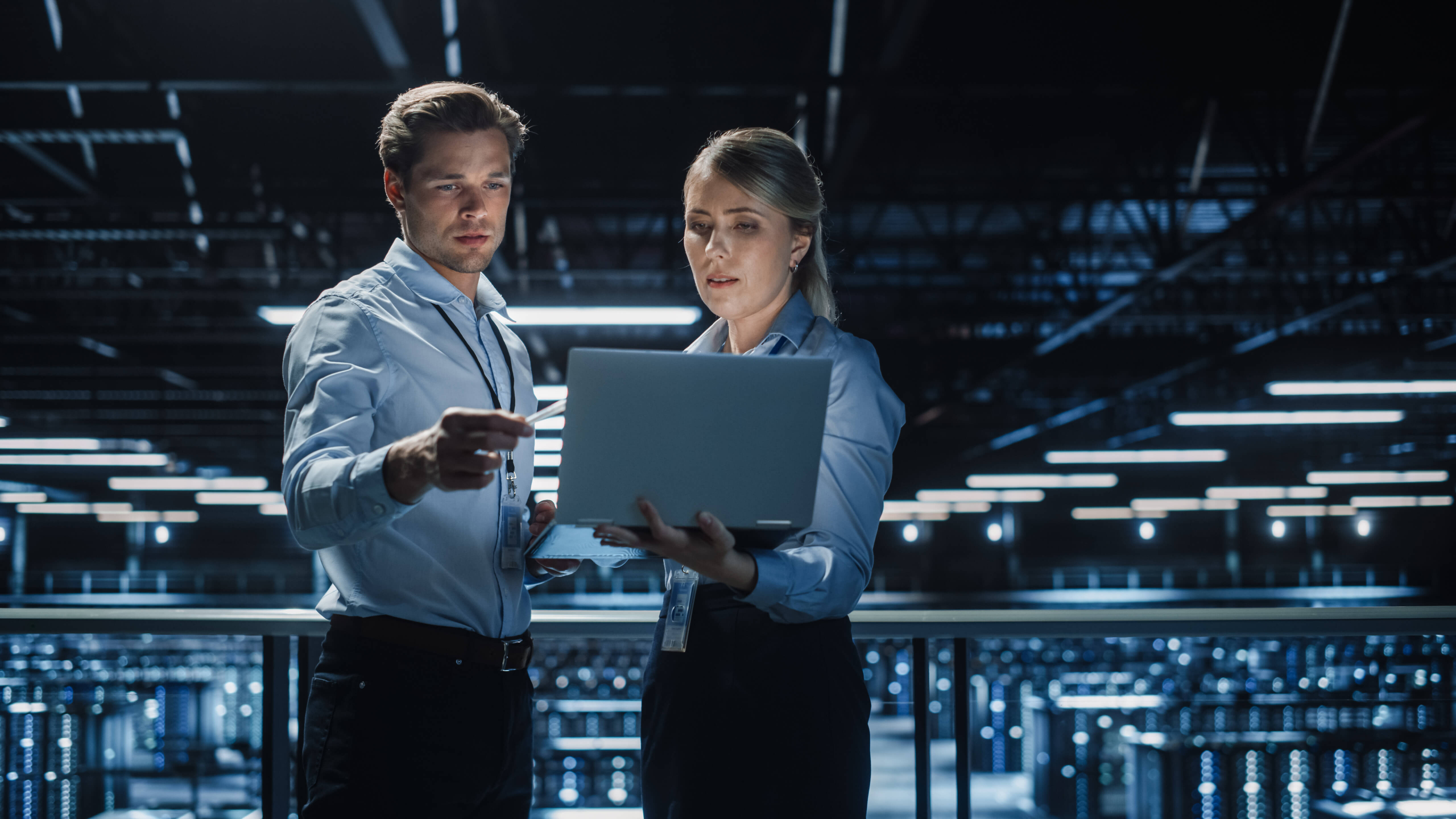 Male and female so workers standing with a laptop and in a server room