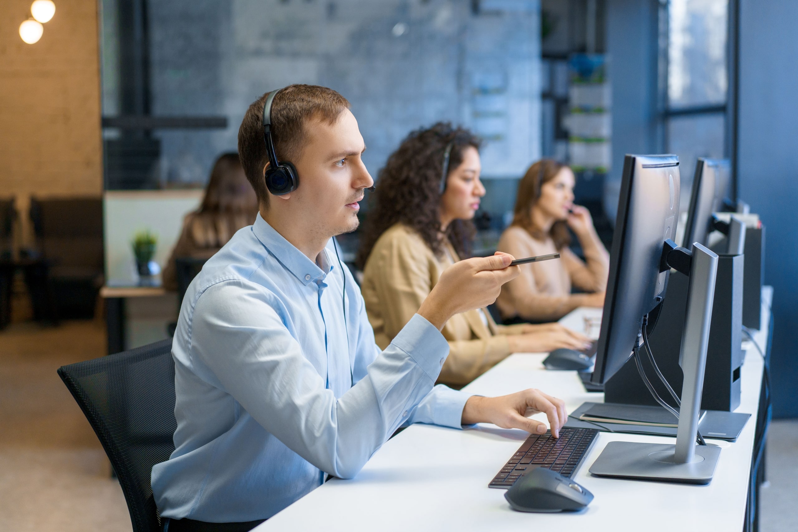 Diverse group of people working at call center or helpful customer service. Busy seller at agency office uses pc computer and answers questions on phone. Friendly man talks on modern hotline closeup
