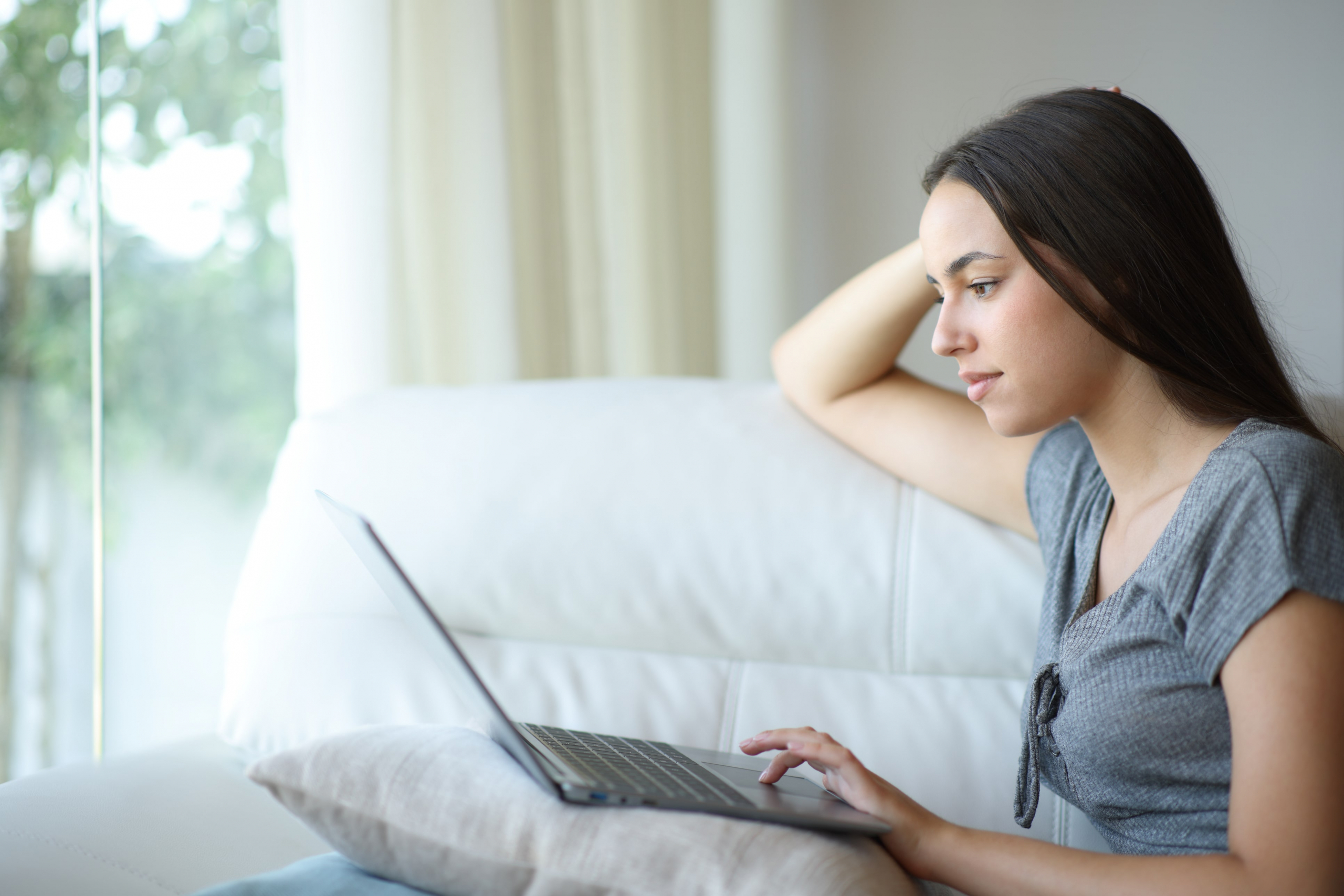Young woman on her couch live chatting on her computer