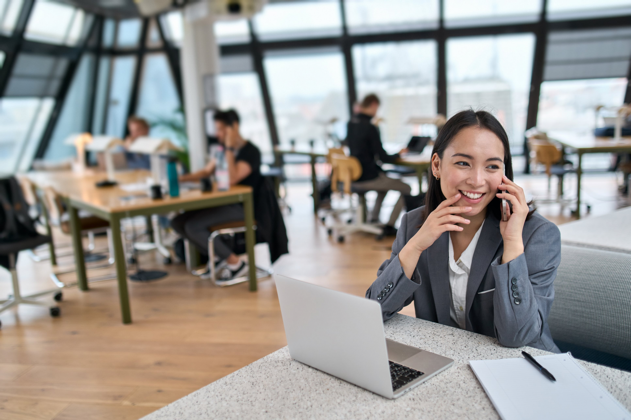 woman sitting in a modern office talking on her phone while at her laptop