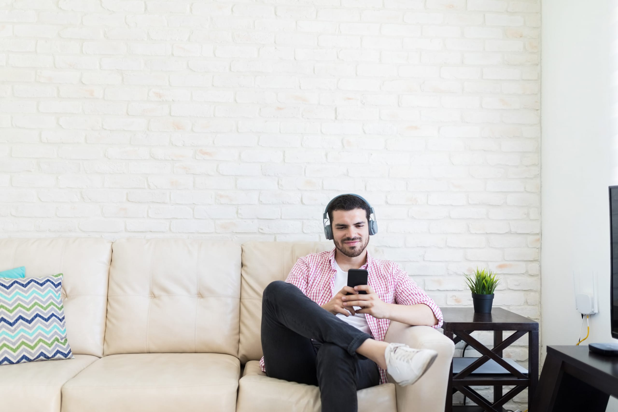 Man sitting on a couch with headphones and watching his phone