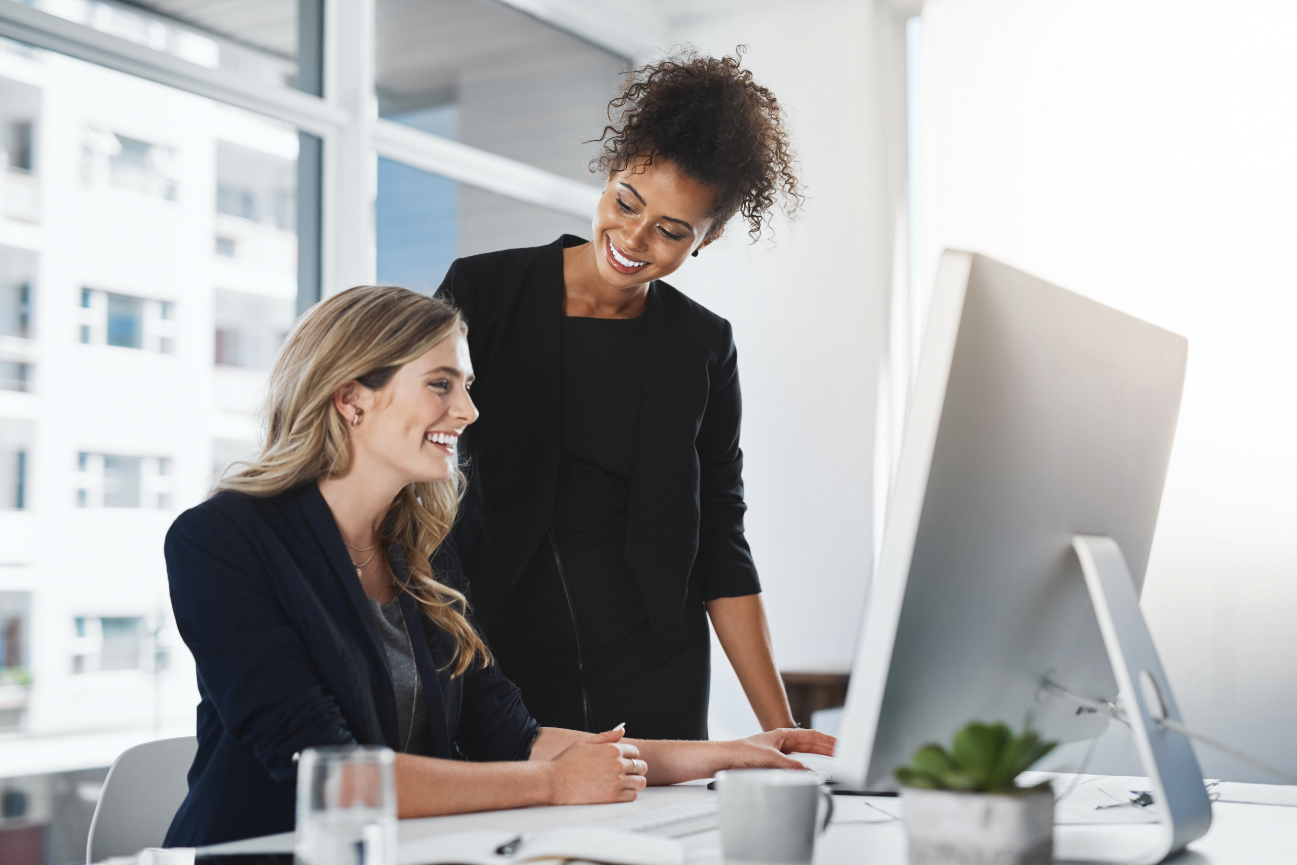2 female co-workers smiling looking at a compter screen