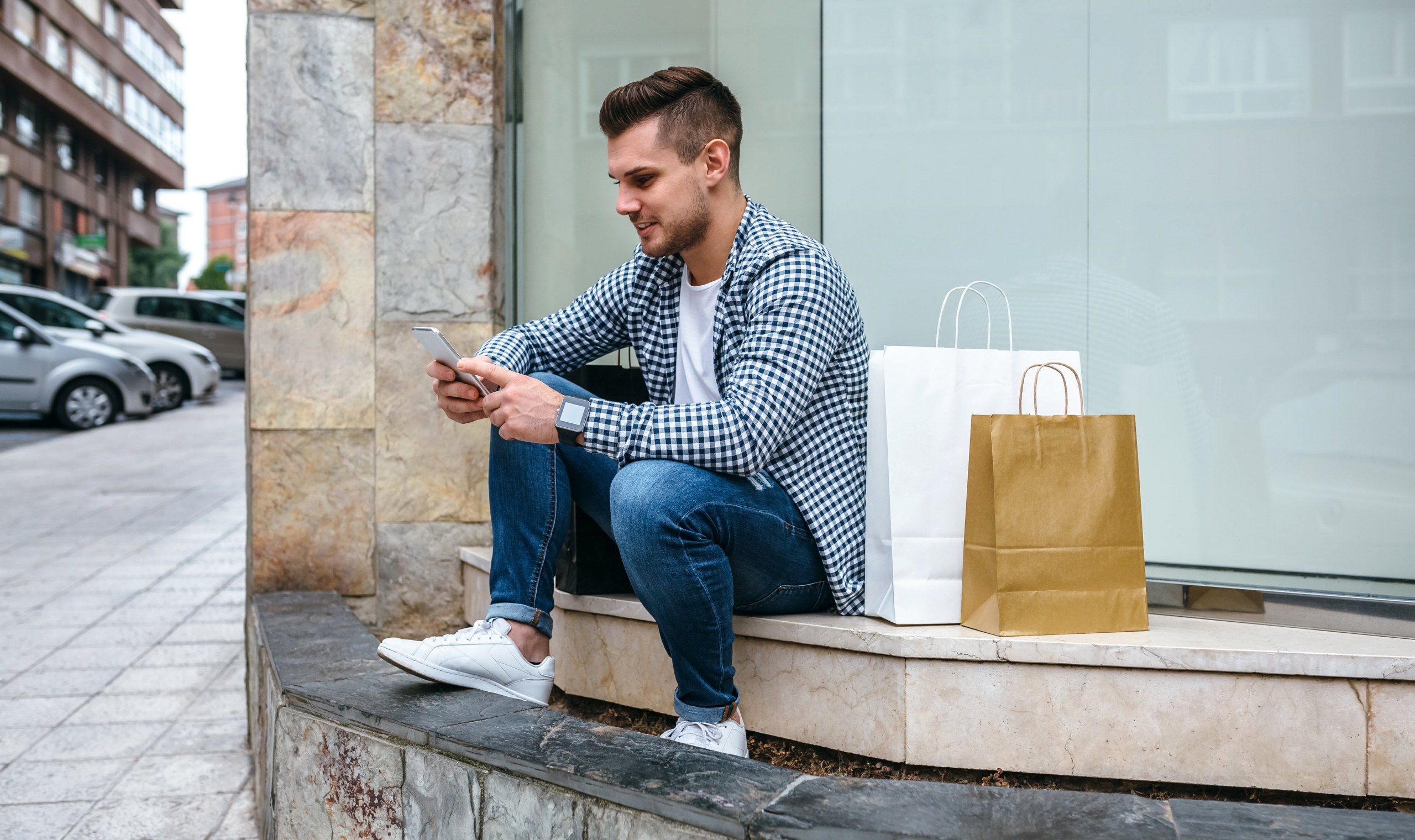 Young man sitting outside on a step chatting on his phone with bags next to him