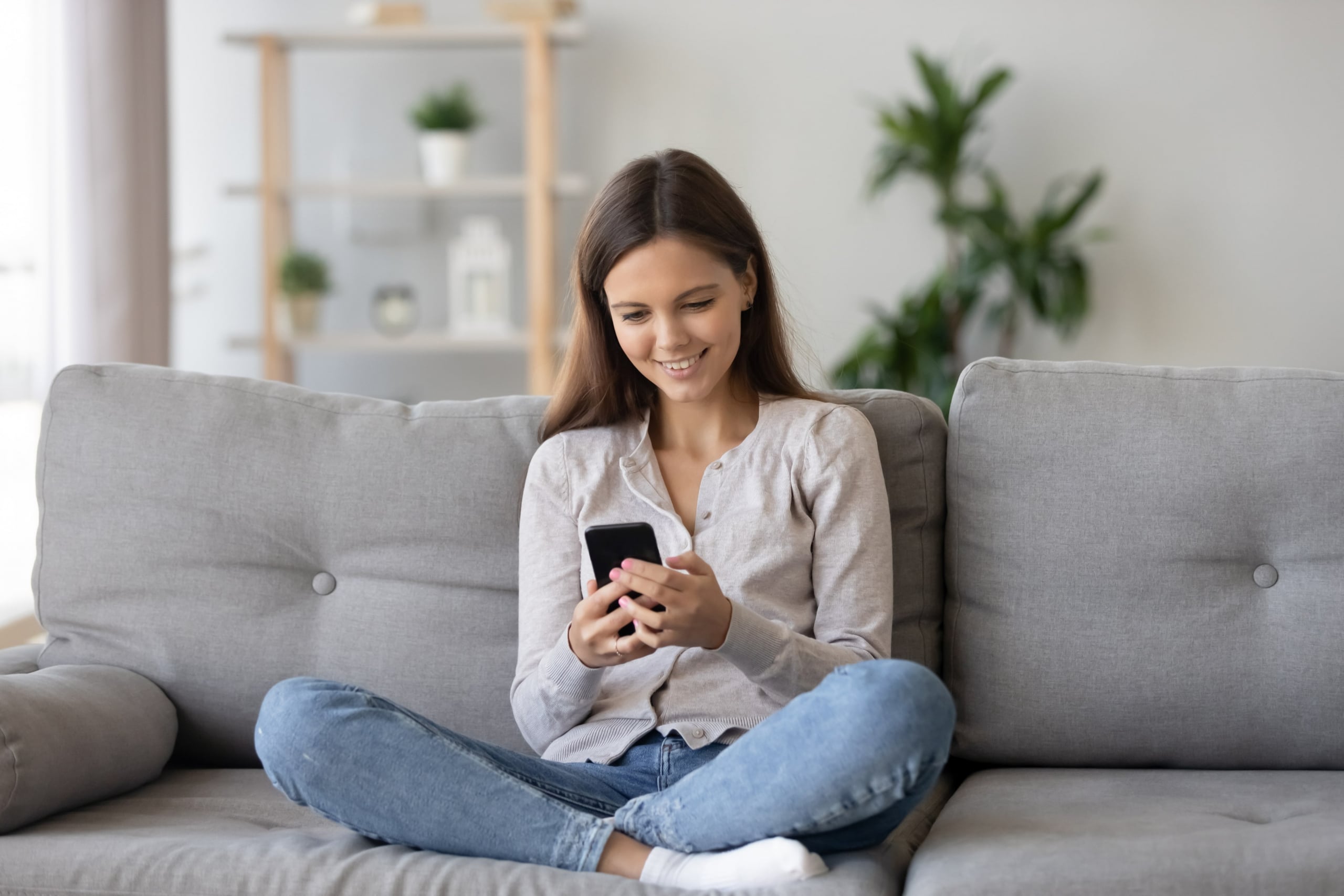 Young woman sitting her couch smiling looking at her cell phone
