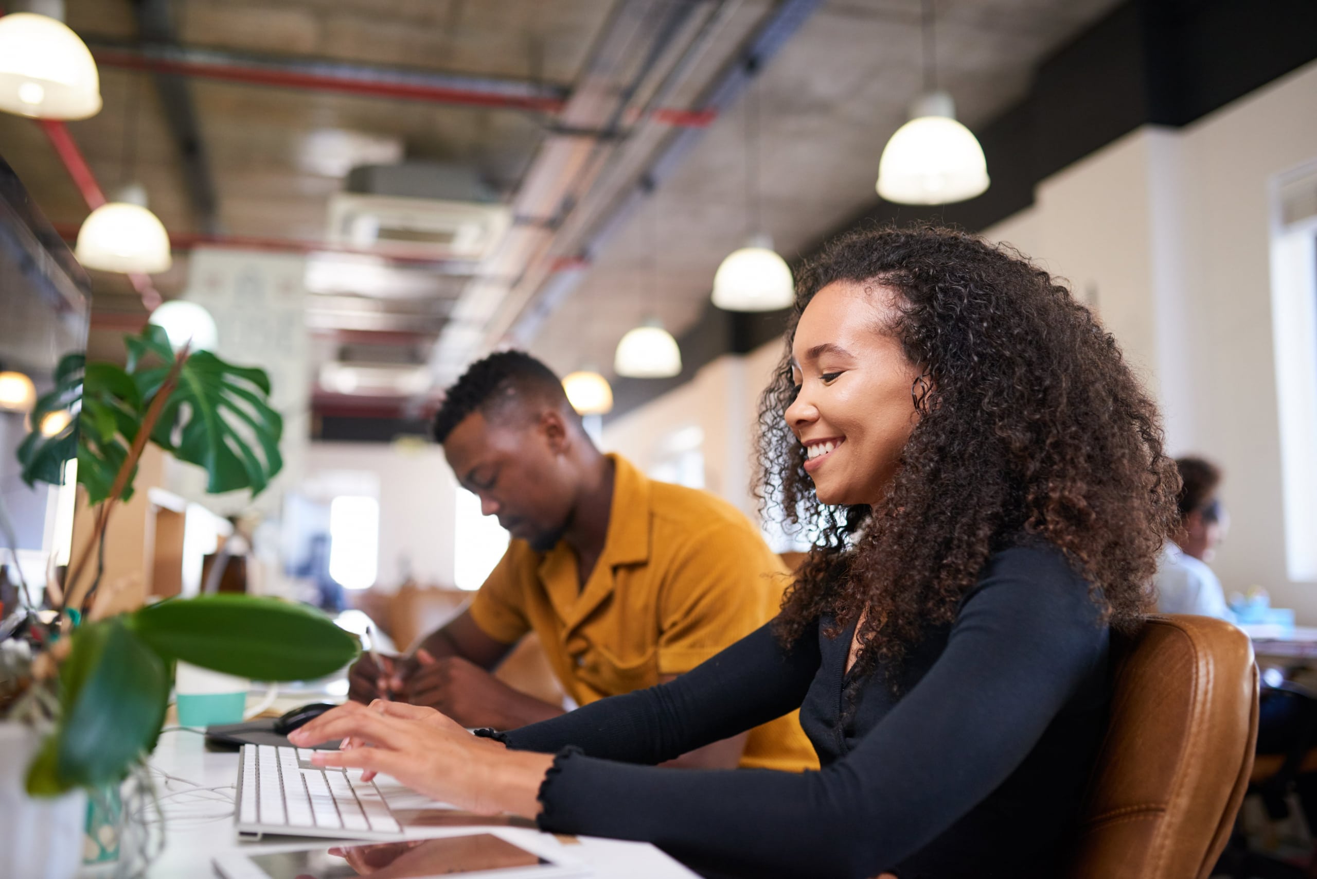 2 African American co-workers smiling working at their desks on computers