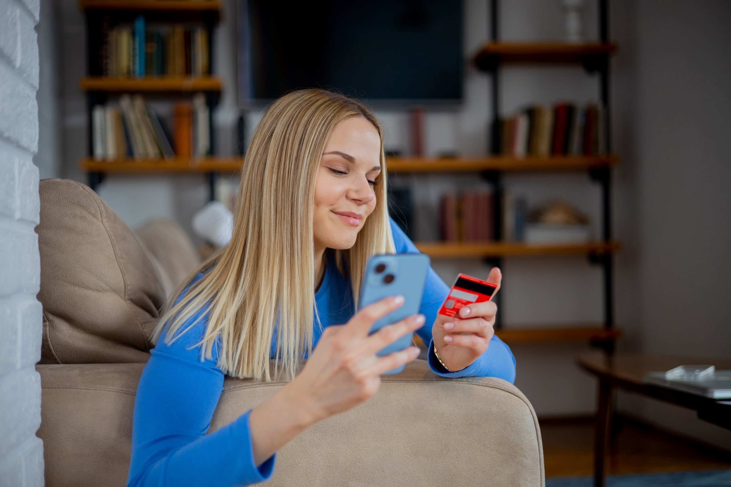 A woman holder her phone and a credit card sitting on her couch