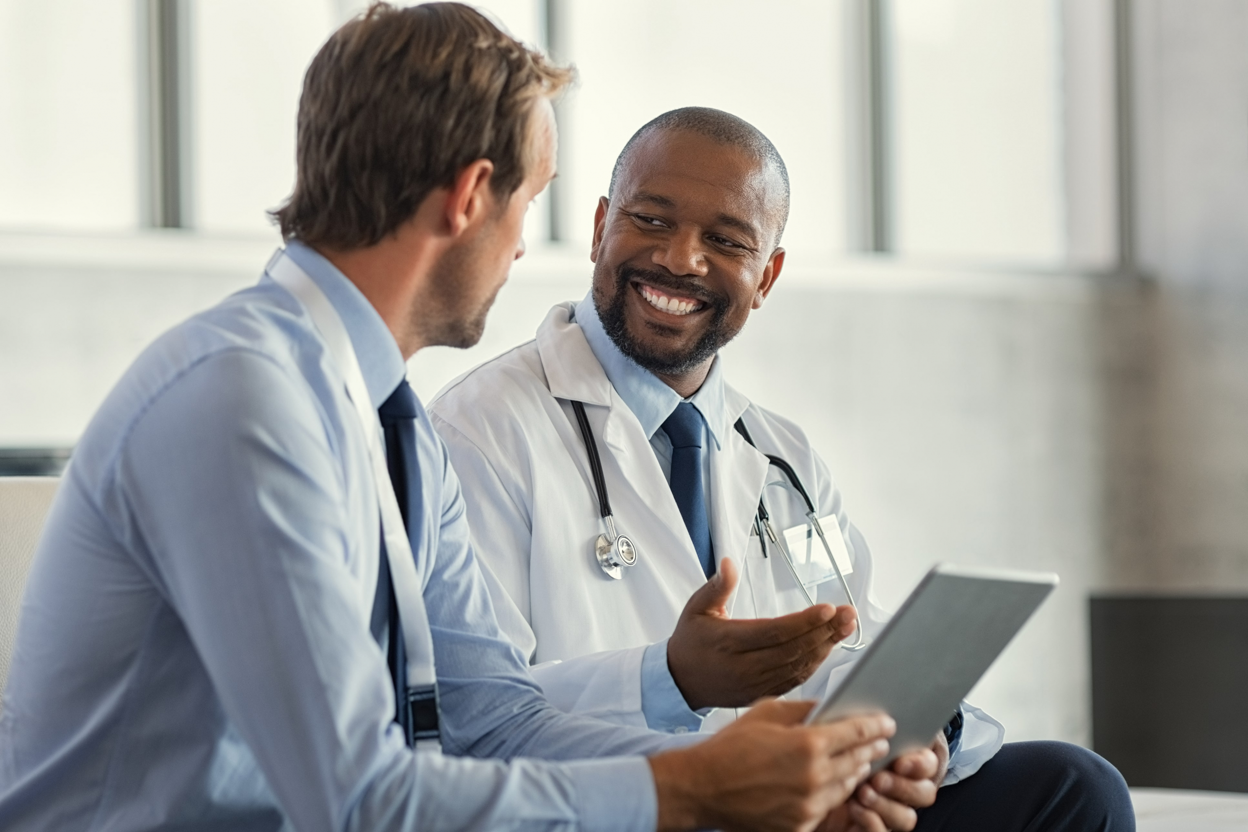 Male doctor and male healthcare administrator talking and smiling looking at a tablet