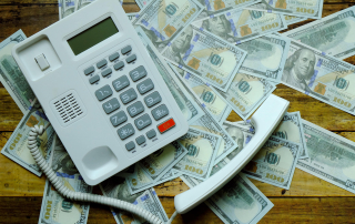 A phone sitting on top of hundred dollar bills illustrating the cost of missed calls.