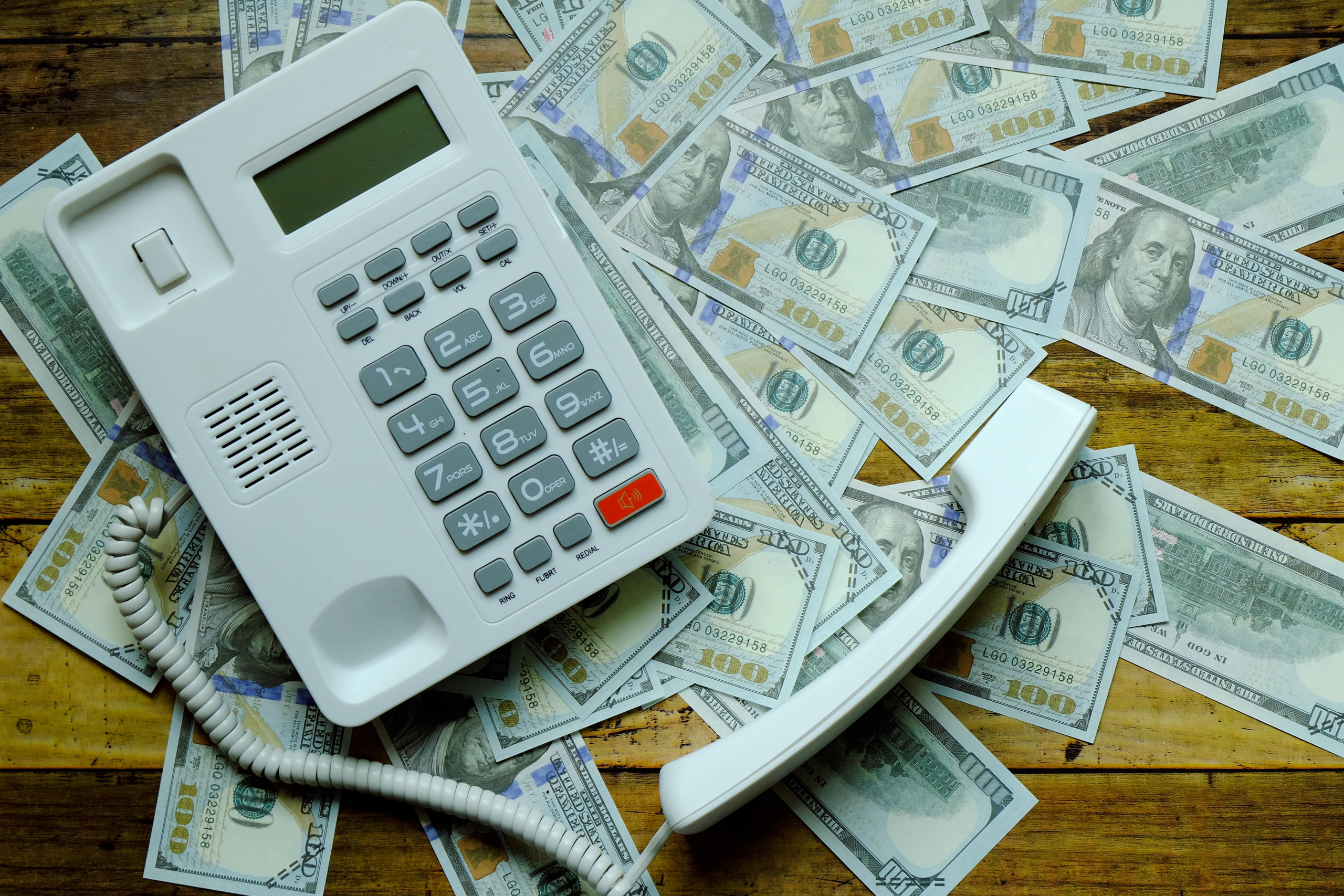 A phone sitting on top of hundred dollar bills illustrating the cost of missed calls.