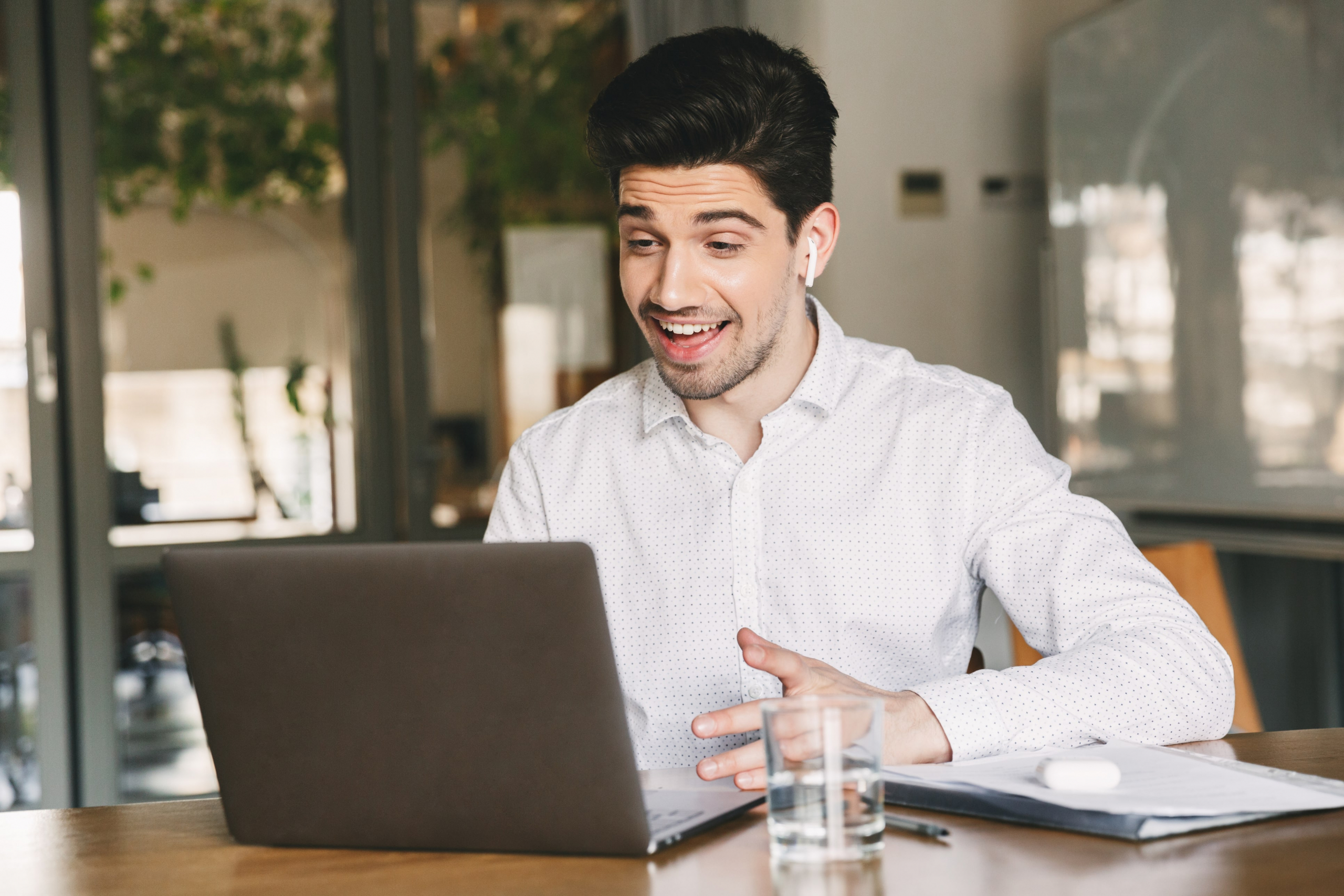 young man talking on his laptop and smiling with earbuds in his ears