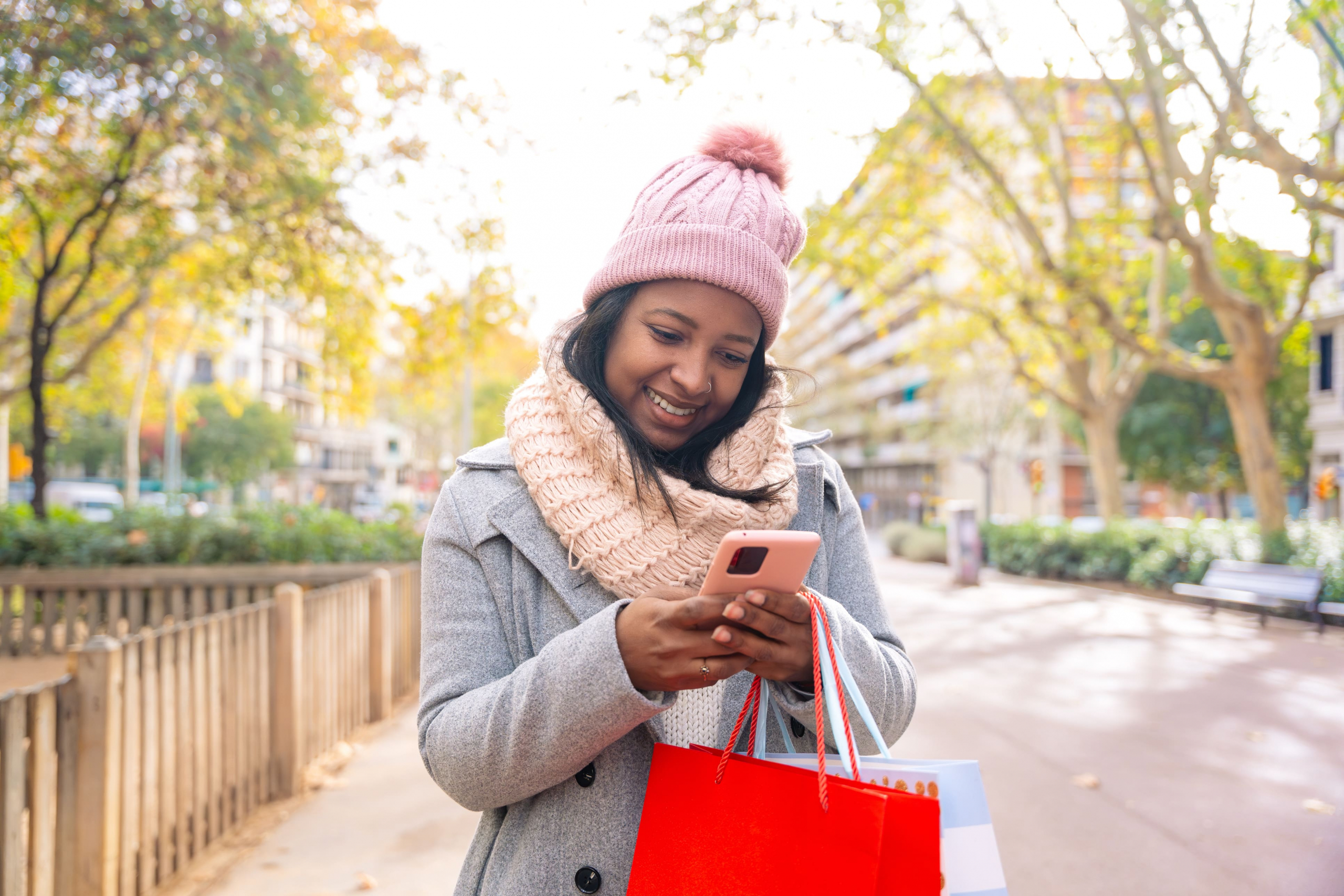 young african-american woman with winter clothes on smiling while typing on her cell phone