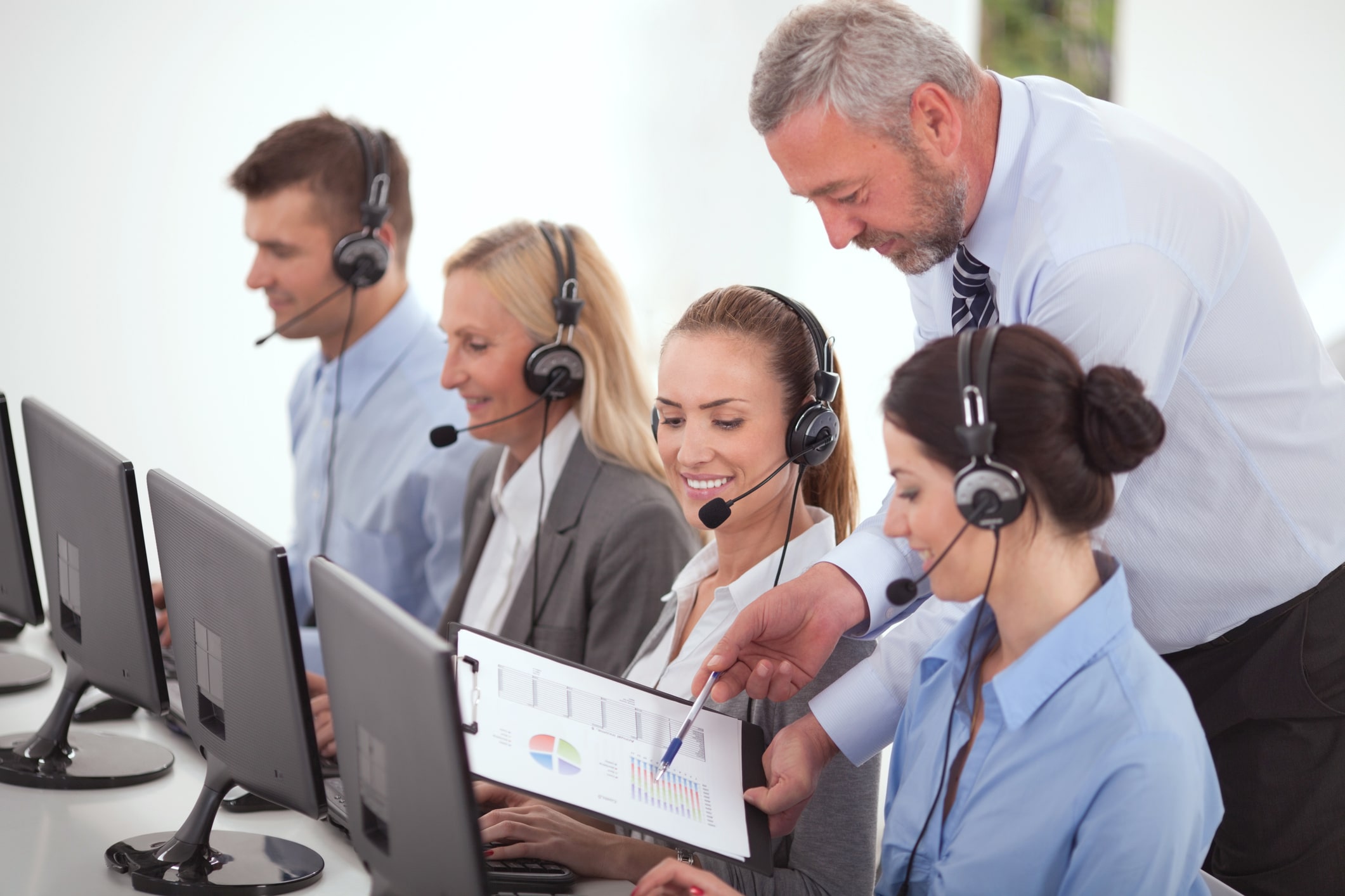 Customer support representatives on the phone and their manager showing them performance charts.
